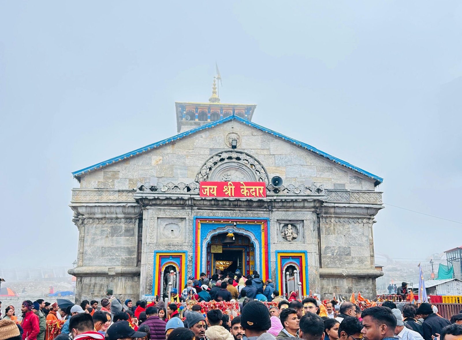 A large crowd gathers at the historic Kedarnath Temple in India amidst misty weather.